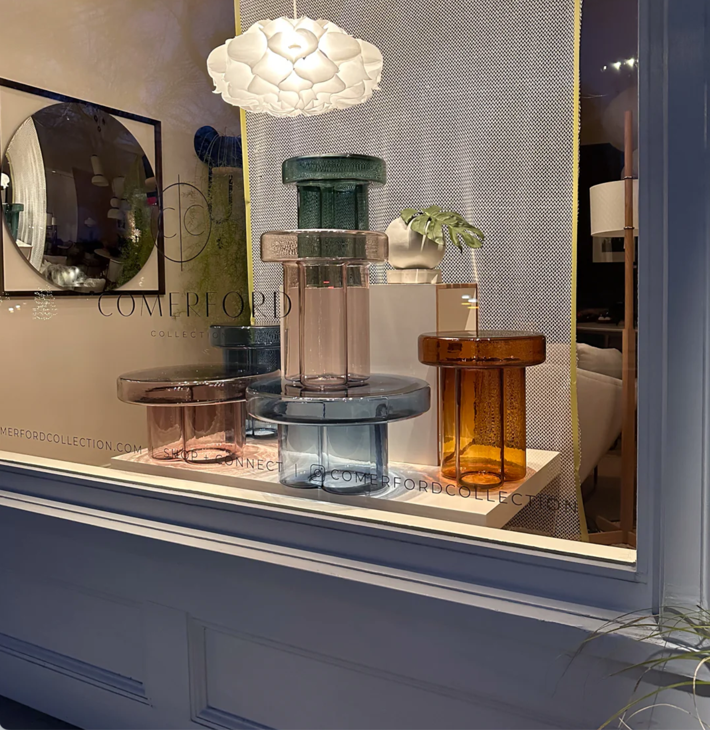 Decorative glass vases on a shelf with a lamp above, in a luxury store window.