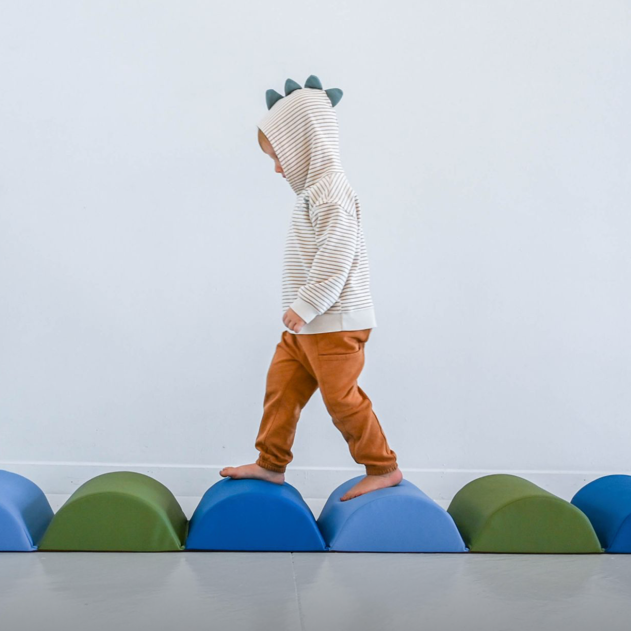Child in a hoodie and brown pants standing on colorful balls against a light  background for Children's Factory.